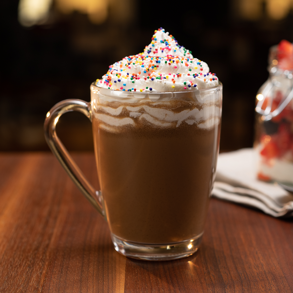 A mug of Hills Bros. Cappuccino Double Mocha Instant Cappuccino Mix with whipped cream and sprinkles, perfect for cappuccino lovers, placed on a table at a coffee house.