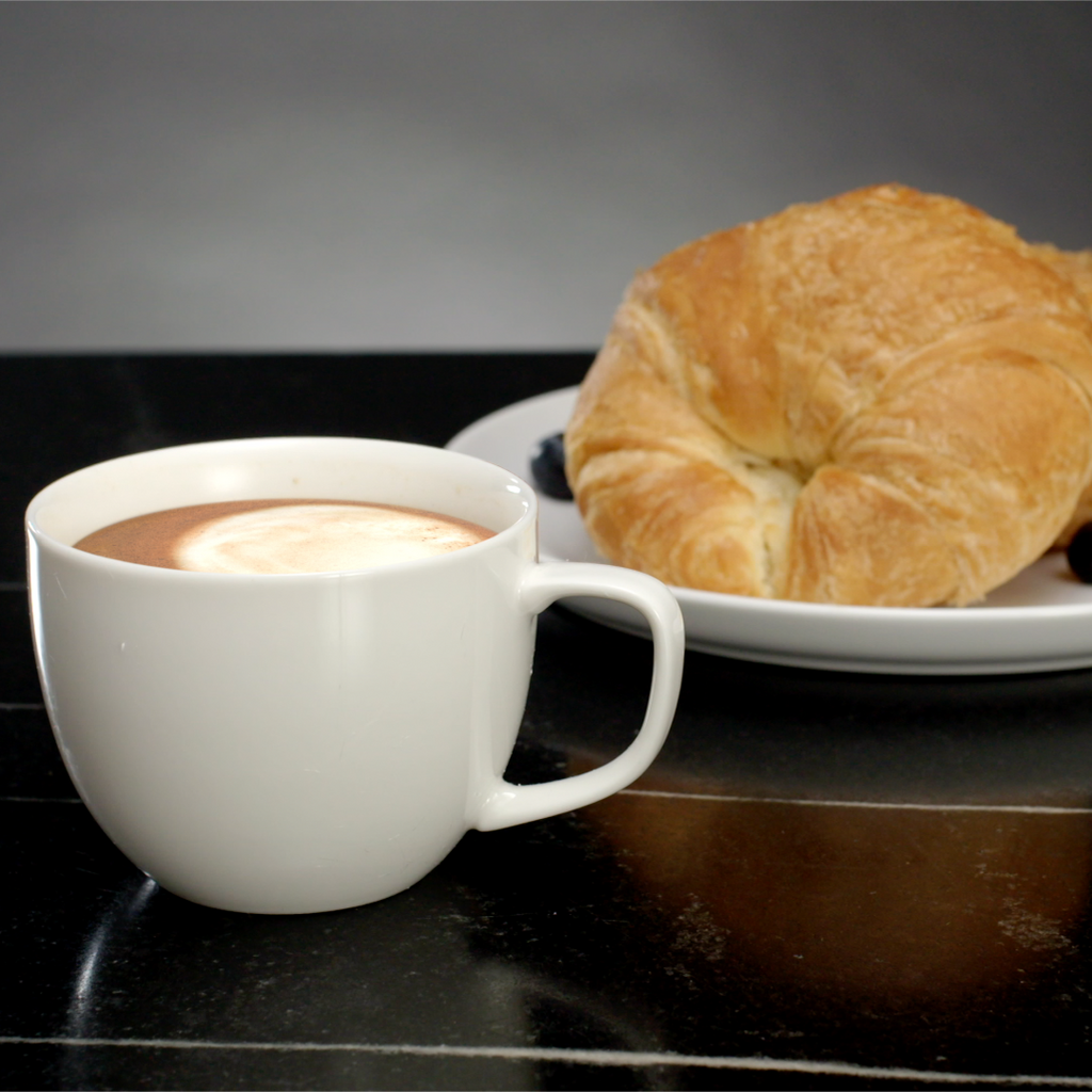 A cup of Double Mocha - Instant Cappuccino Mix sits next to a plate of pastries in a coffee house.
