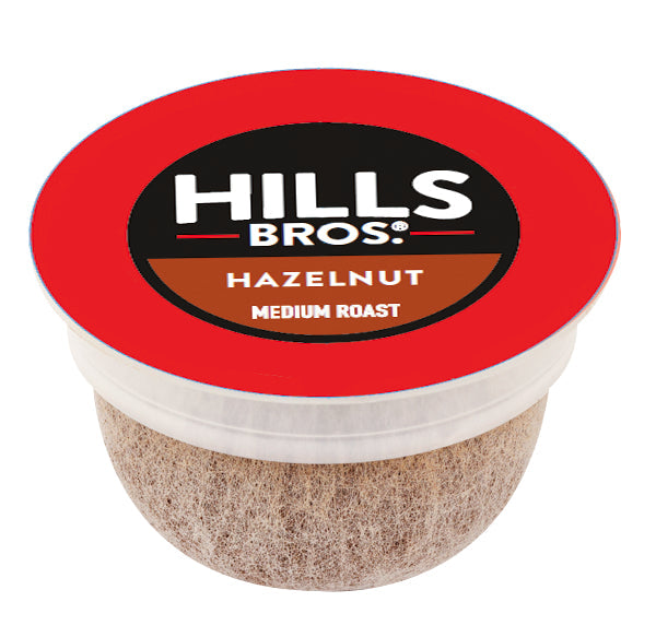 A single-serve coffee pod with a red lid labeled "Hills Bros. Coffee Hazelnut Blend - Medium Roast - Single-Serve Coffee Pods," made from premium arabica beans for an exceptional flavor.