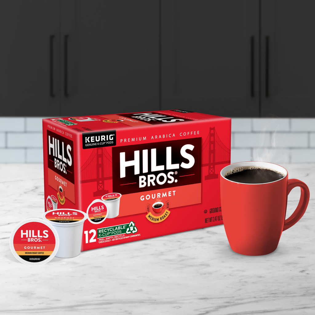 Box of Hills Bros. Coffee Gourmet Blend - Medium Roast Keurig K-Cup® Pods on a counter with a steaming red mug and a single pod in the foreground, showcasing the rich flavor of premium Arabica beans.