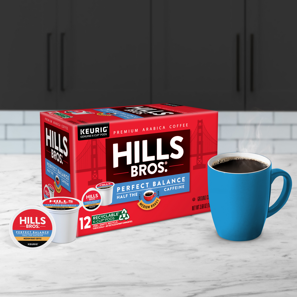 A box of Perfect Balance - Medium Roast K-Cup® Pods from Hills Bros. Coffee sits on the counter beside a steaming blue mug, boasting 12 Keurig-compatible pods made with 100% Arabica beans.