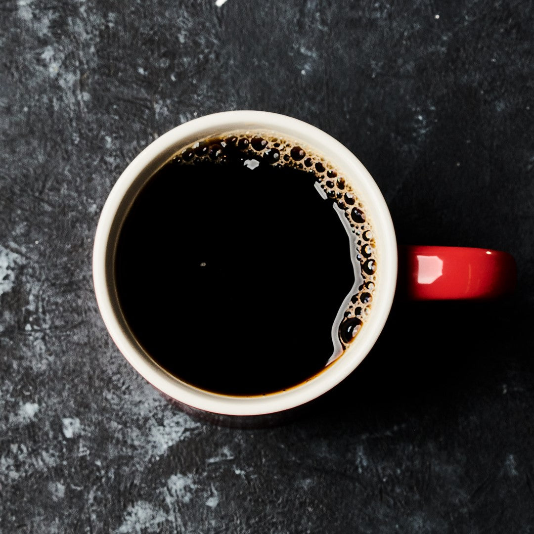 A top view of a red mug filled with Hills Bros. Coffee Colombian - Dark Roast - Ground, placed on a dark textured surface.