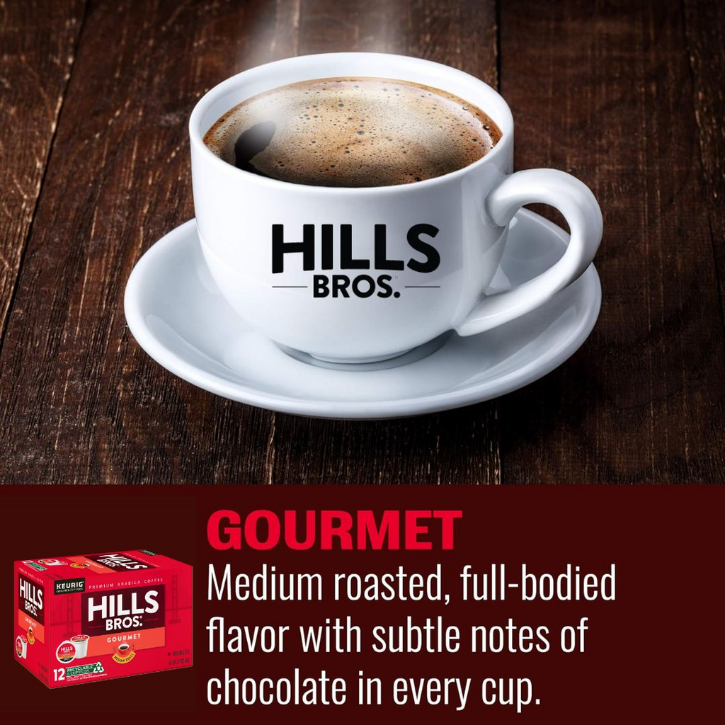 A cup of coffee on a wooden table featuring the label "Hills Bros. Coffee." The caption describes the coffee as Gourmet Blend - Medium Roast - Keurig K-Cup® Pods with a full-bodied flavor and subtle chocolate notes, made from premium Arabica beans.