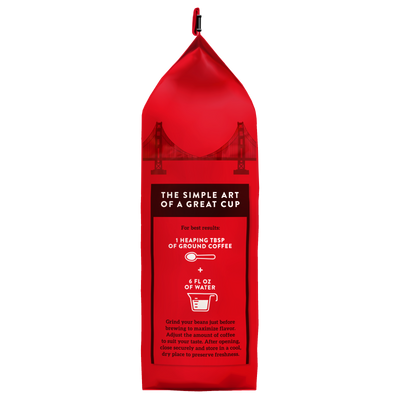 The Hills Bros. Coffee Donut Shop Medium Roast Whole Bean, made from premium Arabica coffee beans, comes in a red bag featuring a Golden Gate Bridge design. Brewing instructions on the bag suggest using 1 heaping tablespoon of ground coffee with 6 fl oz of water, and tips for freshness and storage are provided below the instructions.